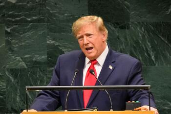 El presidente de los Estados Unidos, Donald Trump, habla desde un podio con micrófonos frente a una pared de mármol verde.