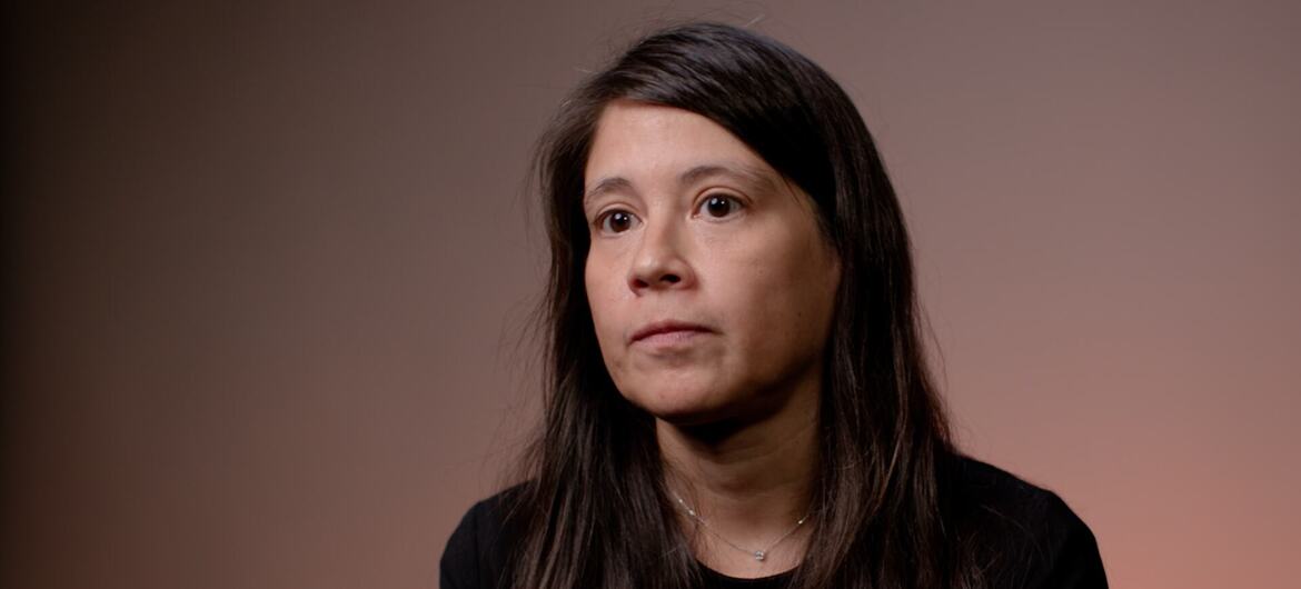 Juana Ibáñez, una mujer de cabello largo y oscuro que viste una blusa negra, mira fuera de cámara contra un fondo de estudio de color marrón apagado.