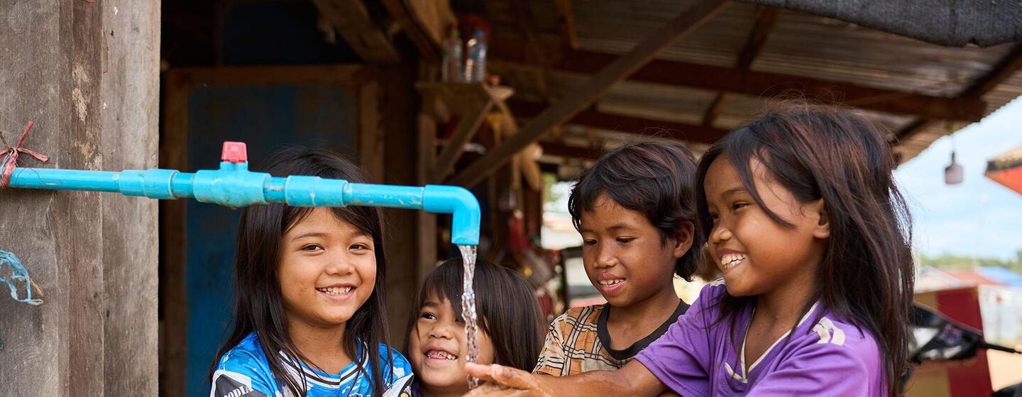 Quatre jeunes filles Jarai, de la communauté autochtone, se lavent les mains sous un robinet à tuyau bleu dans un village rural de la province de Ratanakiri, au Cambodge.
