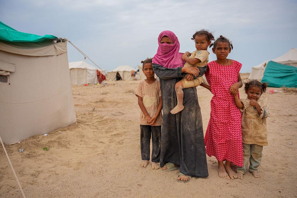 Une femme portant un foulard rose et tenant un bébé se tient avec quatre enfants devant une tente blanche au centre de déplacés d'Al-Firdoss à Aden, au Yémen.