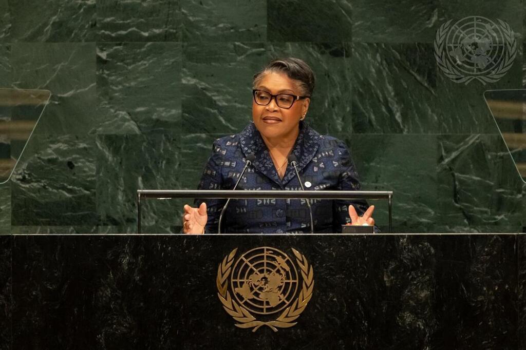 Mwanamke Mweusi aliyevaa miwani na koti la bluu lenye muundo akizungumza kwenye jukwaa la UMOJA WA MATAIFA lenye nembo UN , huku kuta za marumaru ya kijani nyuma yake wakati wa kikao cha Baraza Kuu.