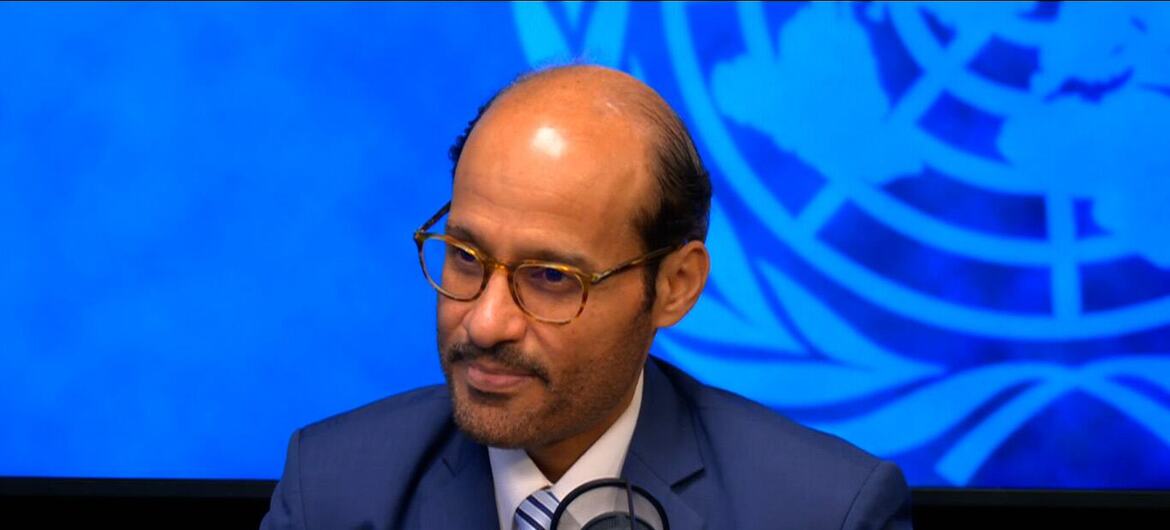 الدكتور محمد الكويتي، مرتدياً نظارة وبدلة زرقاء، يتحدث في ميكروفون أمام خلفية زرقاء للأمم المتحدة.