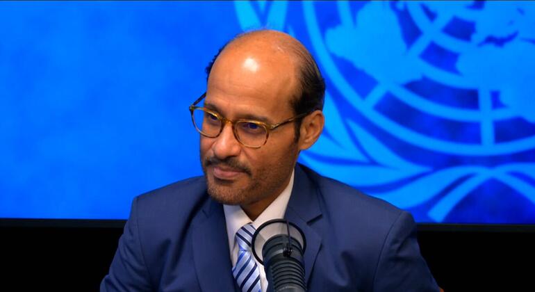 الدكتور محمد الكويتي، مرتدياً نظارة وبدلة زرقاء، يتحدث في ميكروفون أمام خلفية زرقاء للأمم المتحدة.