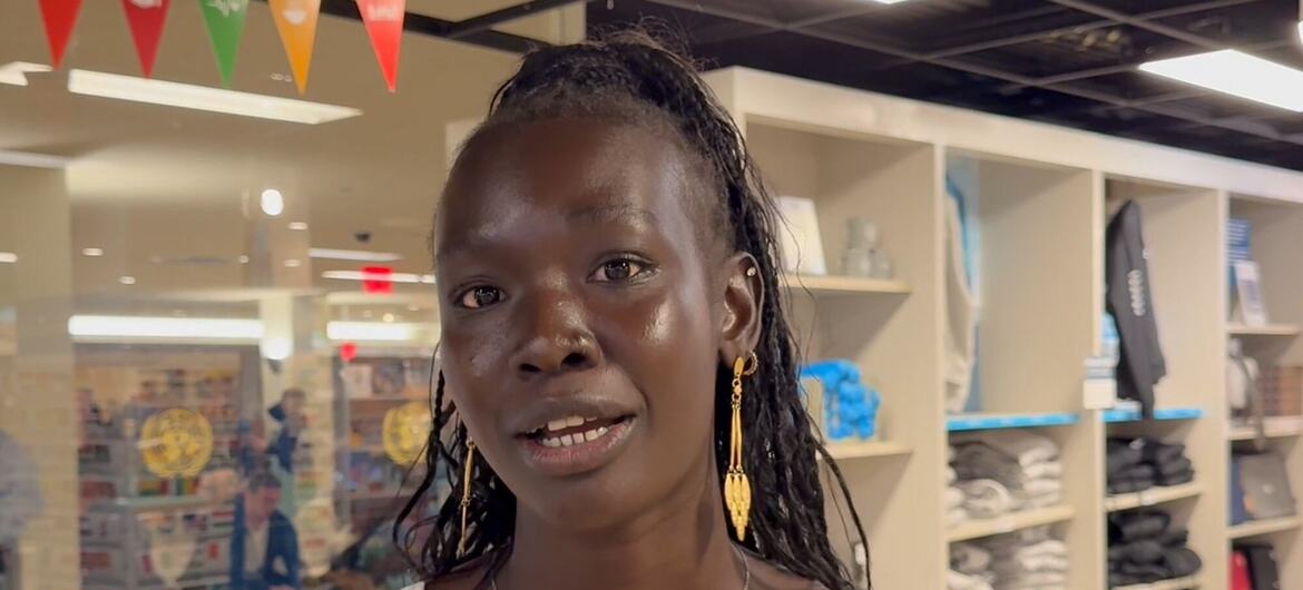 Mwanamke Mweusi mwenye nywele zilizosokotwa na hereni za dhahabu anaongea akiwa amesimama katika duka la nguo lenye rafu za nguo zilizokunjwa.