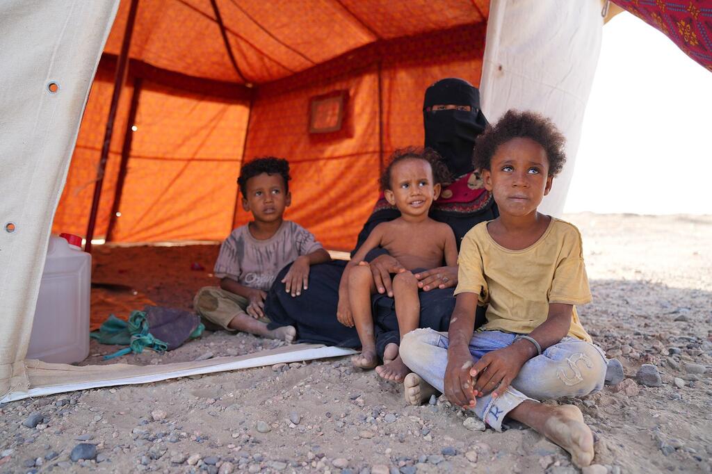 Une mère yéménite portant le niqab est assise avec quatre jeunes enfants à l'entrée d'une tente orange d'abri d'urgence dans le camp de déplacés d'Al-Firdous, à Aden, au Yémen.