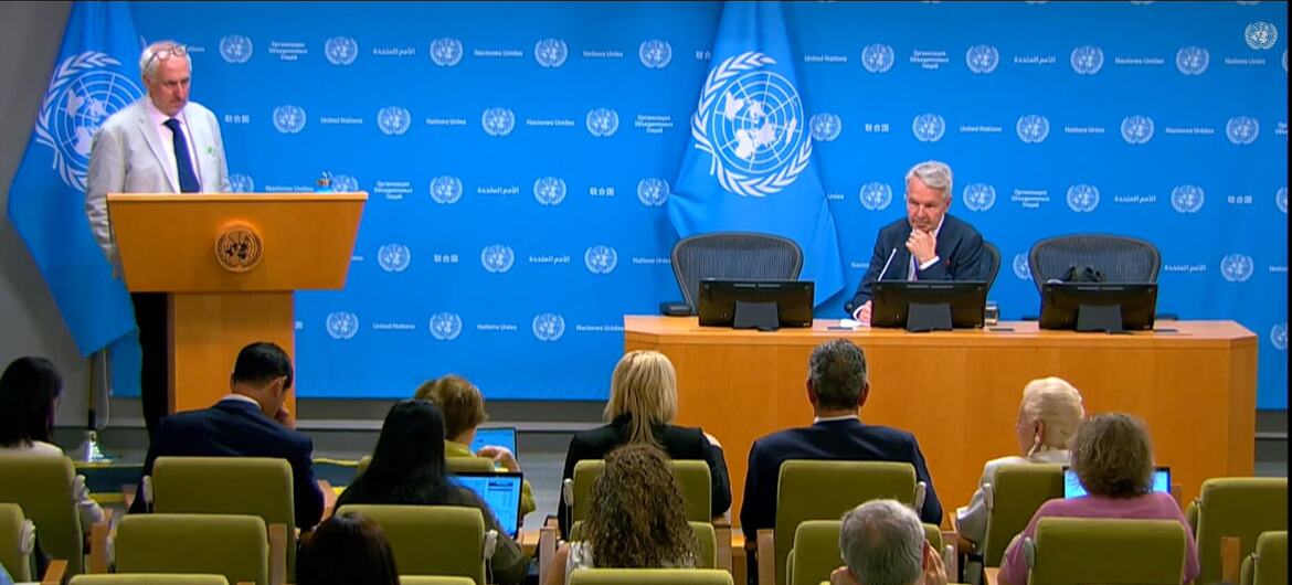 يتحدث بيكا هافيستو على منصة United Nations خلال مؤتمر صحفي، بينما يجلس مسؤول على الطاولة والصحفيون في المقدمة.