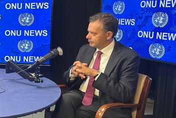 Durante uma entrevista, Luis Montenegro está sentado a uma mesa com um microfone de estúdio em frente a painéis azuis que exibem o texto da ONU News e emblemas das Nações Unidas .