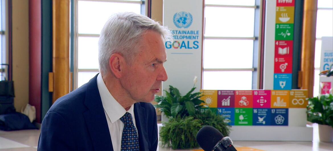رجل ذو شعر رمادي يرتدي بدلة داكنة يُجرى معه مقابلة عبر الميكروفون أمام عرض لأهداف United Nations للتنمية المستدامة.