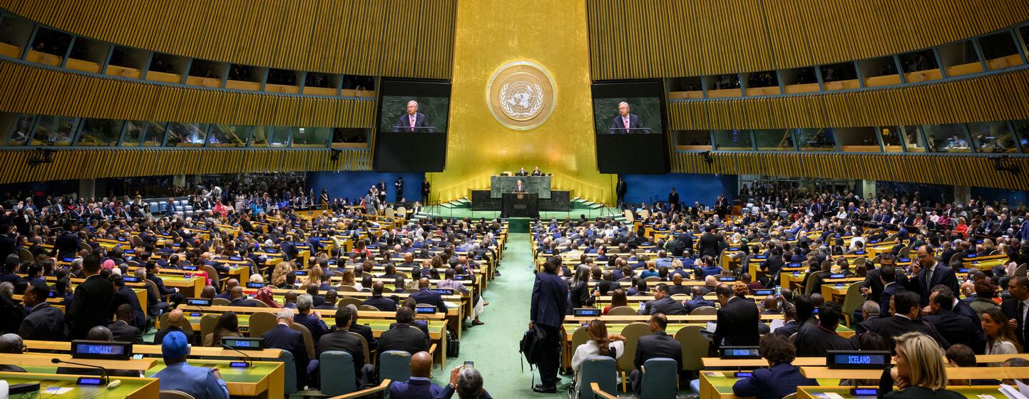 UN Secretary-General António Guterres speaks from a podium in the United Nations General Assembly Hall during the opening of the eighty-first session, with delegates seated and his image on two screens.