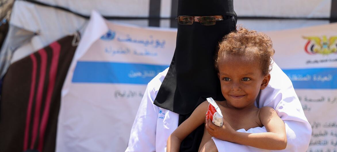 Une agente de santé en niqab noir tient le petit Ghaith qui tient un paquet d'aliments thérapeutiques prêts à l'emploi dans un camp de personnes déplacées à Jabal Habashi, Taiz, au Yémen.