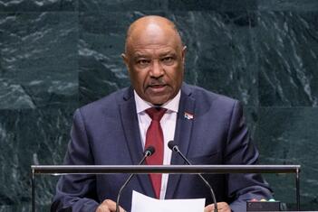 Mwanamume mweusi aliyevaa suti ya bluu nyeusi na tai nyekundu akizungumza kwenye jukwaa la Mkutano Mkuu UMOJA WA MATAIFA akiwa na maikrofoni, dhidi ya mandhari ya marumaru ya kijani kibichi.