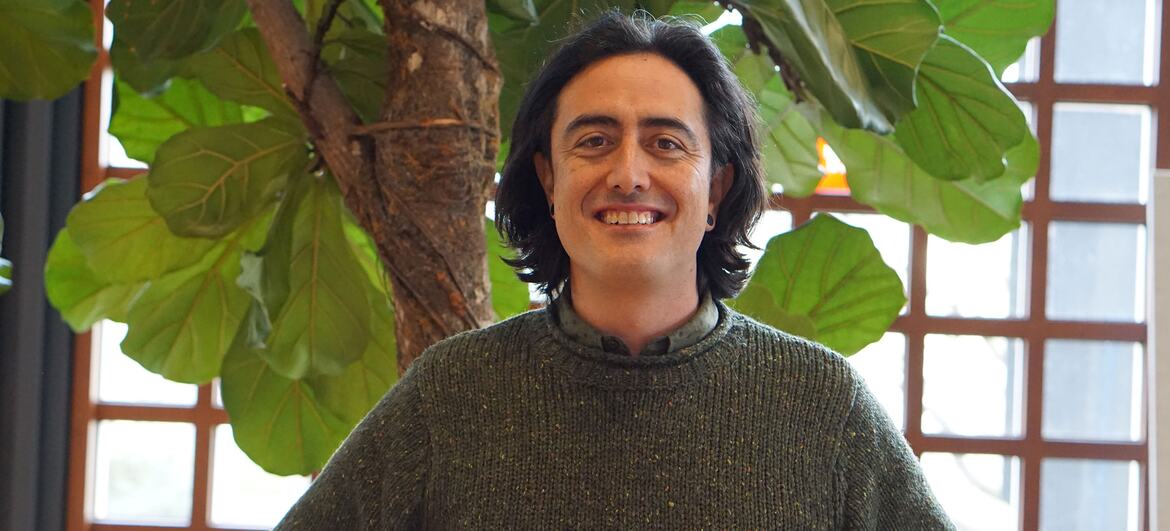 Dr. Jack O'Connor, marine ecologist at UNU-EHS, smiles while standing in front of a large leafy plant and a window.