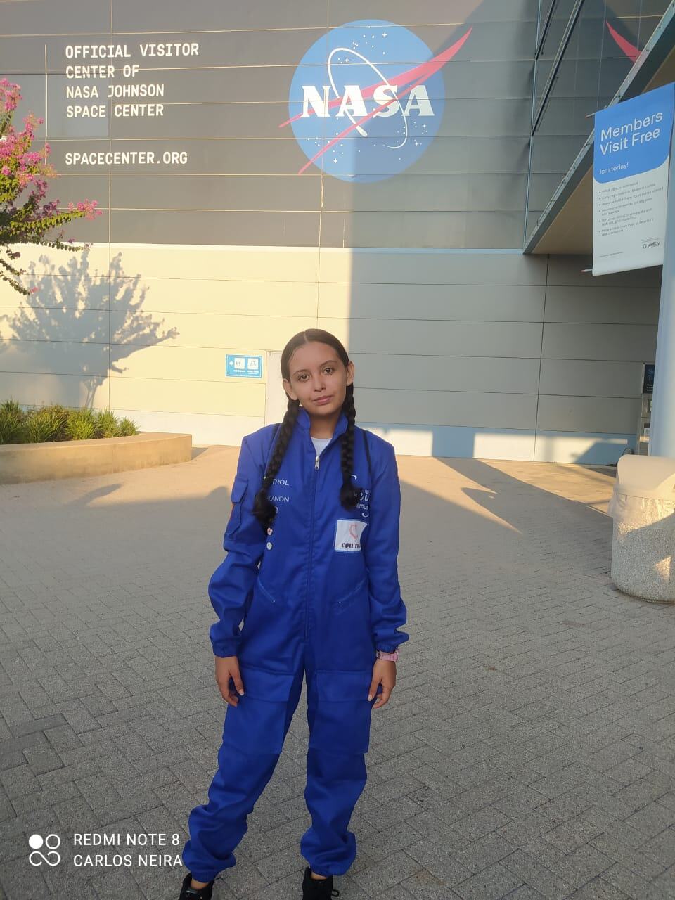 Una joven latina vestida con un mono azul posa frente al centro de visitantes del Centro Espacial Johnson de la NASA .