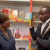 Mwanamke Mweusi aliyevaa koti la kijivu na mwanaume Mweusi aliyevaa koti jeusi lenye mapambo ya dhahabu wamesimama wakitazamana mbele ya rafu za maduka ya vitabu zilizojaa vitabu vya watoto na vijana vyenye rangi mbalimbali.