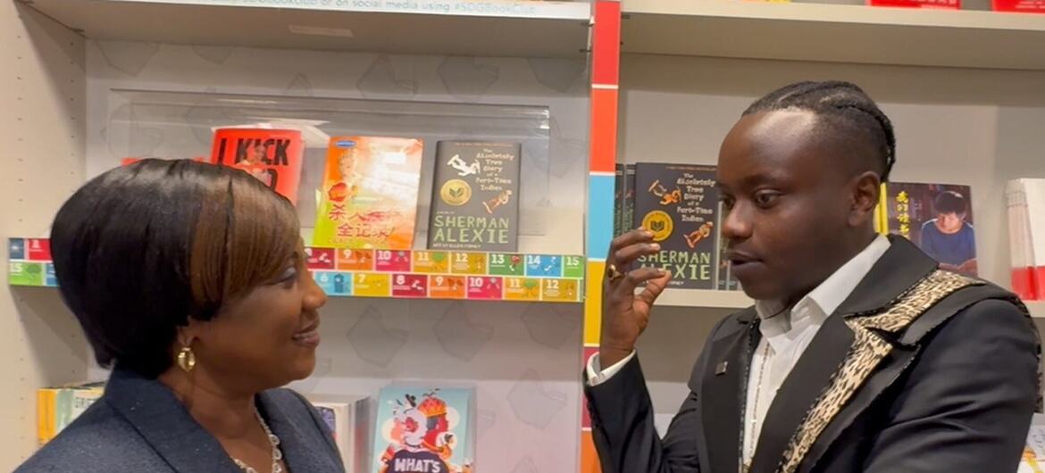 Mwanamke Mweusi aliyevaa koti la kijivu na mwanaume Mweusi aliyevaa koti jeusi lenye mapambo ya dhahabu wamesimama wakitazamana mbele ya rafu za maduka ya vitabu zilizojaa vitabu vya watoto na vijana vyenye rangi mbalimbali.