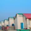 Hilera de casas de una sola planta de reciente construcción, con paredes color crema, techos rojos, detalles en verde y puertas azules, en un asentamiento arenoso en Bosaso, Somalia.