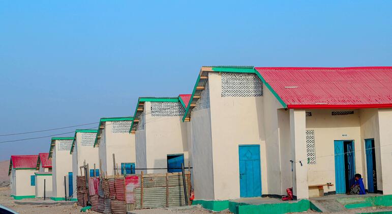 Hilera de casas de una sola planta de reciente construcción, con paredes color crema, techos rojos, detalles en verde y puertas azules, en un asentamiento arenoso en Bosaso, Somalia.