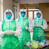 Trois soignants, entièrement équipés de protections individuelles, se tiennent dans un couloir d'hôpital à côté d'un chariot de matériel médical.