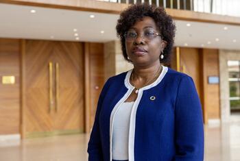 Dr. Neema Rusibamayila Kimambo, a woman with short curly hair and glasses stands in a modern office lobby wearing a blue cardigan over a white top.