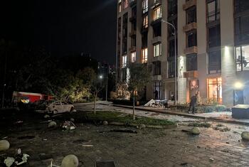 Vue nocturne d'un immeuble résidentiel à Kyiv, en Ukraine, avec des débris, des vitres brisées et une voiture calcinée dans la rue, témoignant des conséquences d'une attaque.