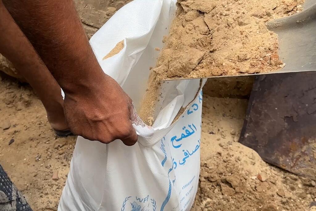 À Gaza, les mains d'une personne déplacée tiennent ouverts un sac tissé blanc dans lequel on verse du sable à l'aide d'une pelle pour créer des digues autour des abris.