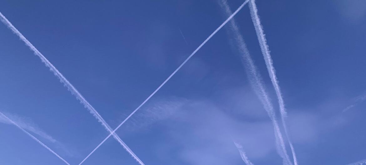 Multiple white aircraft contrails cross a bright blue sky with faint wispy clouds.