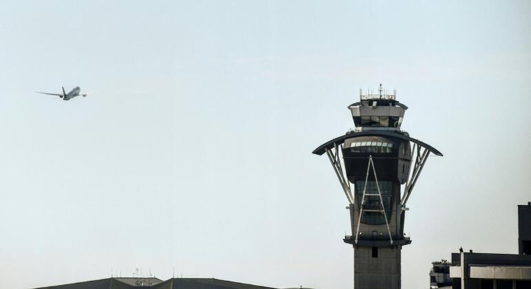 Un avión comercial vuela cerca de una torre de control de aeropuerto bajo un cielo despejado