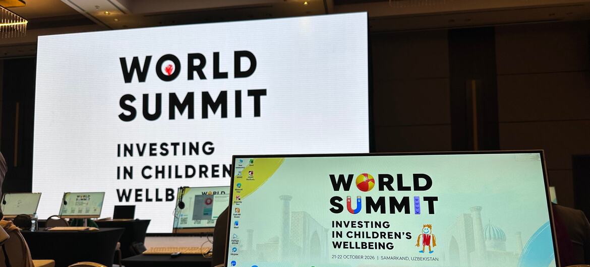 A large screen and a monitor display World Summit Investing in Children's Wellbeing branding for 21-22 October 2026 in Samarkand, Uzbekistan, with QR codes for media resources and Wi-Fi access in a conference room.