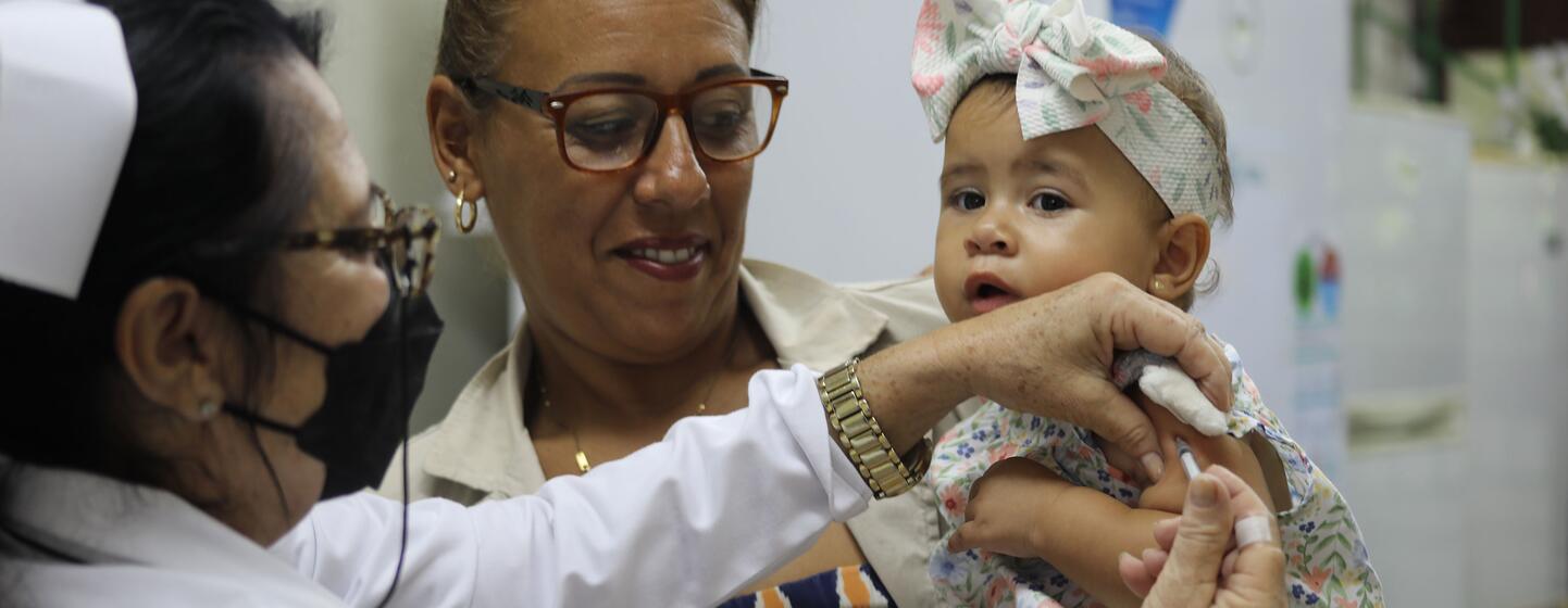 Una enfermera administra una vacuna a un bebé en manos de una mujer, mostrando el trabajo sanitario de la ONU en Cuba.