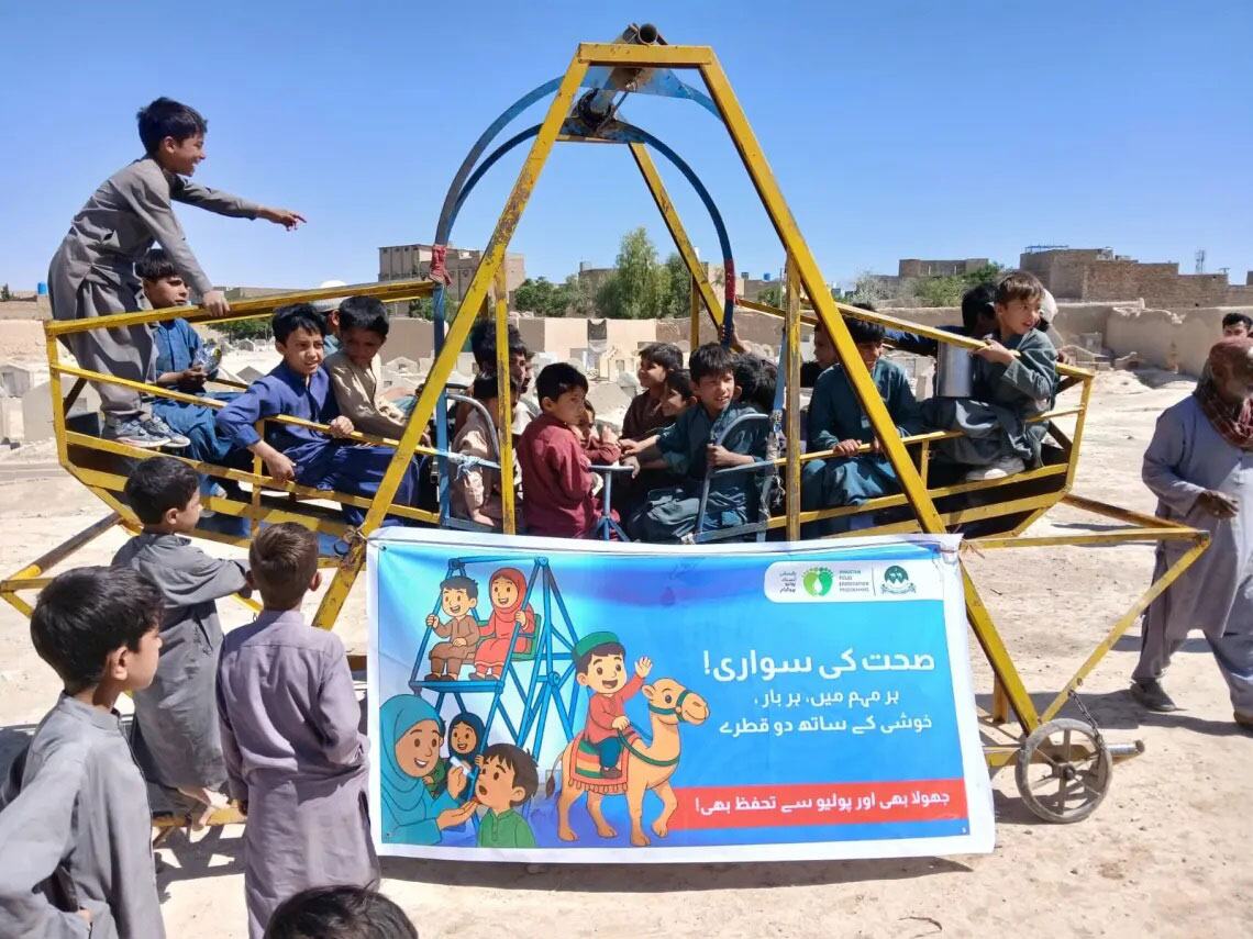 بلوچستان، پاکستان میں بچے پولیو ویکسینیشن حاصل کرنے کے لیے یونیسف اور جاپان کی مدد سے 'Immunity Express' نامی رنگین موبائل ویکسینیشن یونٹ پر سوار ہوتے ہیں۔ یہ بینر مقامی زبان میں بچوں کی صحت اور ویکسینیشن کو فروغ دیتا ہے۔