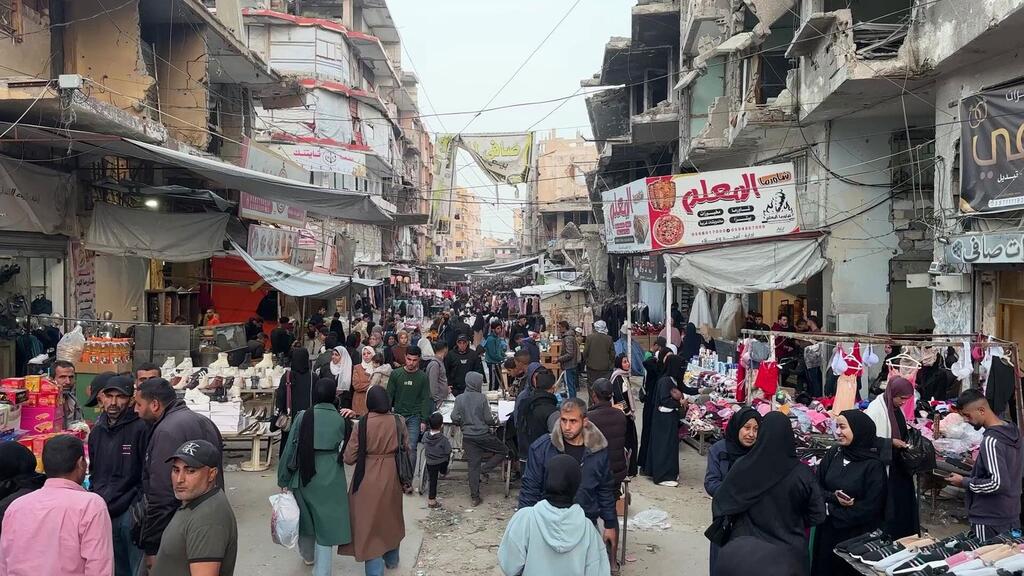 Un marché de rue bondé à Khan Younis, à Gaza, avec des hommes, des femmes et des enfants palestiniens faisant leurs courses au milieu d'immeubles endommagés par la guerre.