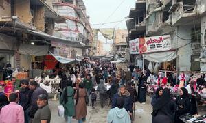 A crowded street market in Khan Younis, Gaza, with Palestinian men, women and children shopping amidst buildings damaged by war.
