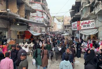 A crowded street market in Khan Younis, Gaza, with Palestinian men, women and children shopping amidst buildings damaged by war.