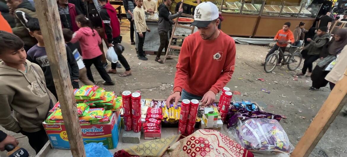 Un jeune Palestinien vêtu d'un pull rouge et d'une casquette blanche vend des collations et des bonbons depuis un stand improvisé dans un marché bondé de Khan Younis, à Gaza.