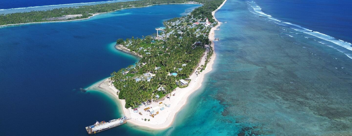 Aerial view of the island nation of Tuvalu showing its narrow strip of land surrounded by a vibrant turquoise lagoon and deep blue ocean, highlighting the effects of coastal erosion and climate change.