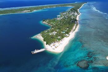 Aerial view of the island nation of Tuvalu showing its narrow strip of land surrounded by a vibrant turquoise lagoon and deep blue ocean, highlighting the effects of coastal erosion and climate change.