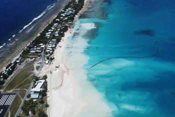 Aerial view of a sand replenishment project in Tuvalu to combat coastal erosion, showing a dredging vessel and new sand deposits along the shoreline.