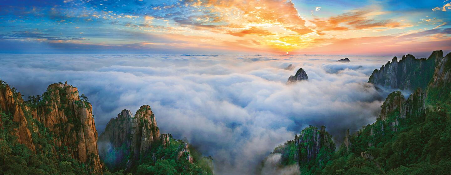 Vista panorámica de la reserva de la biosfera del monte Huangshan en China al amanecer, con montañas cubiertas de niebla y un cielo vibrante.