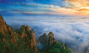 Panoramic view of Mount Huangshan biosphere reserve in China at sunrise, with mist-covered mountains and vibrant sky.