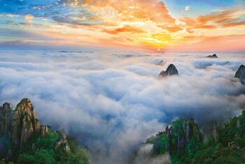 Vue panoramique de la réserve de biosphère du mont Huangshan en Chine au lever du soleil, avec des montagnes couvertes de brume et un ciel vibrant.