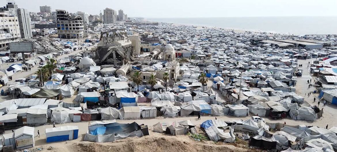 صورة جوية لمخيم كبير للاجئين مع العديد من الخيام التي أقيمت بالقرب من الساحل في غزة، محاطة بالأنقاض والمباني المدمرة.