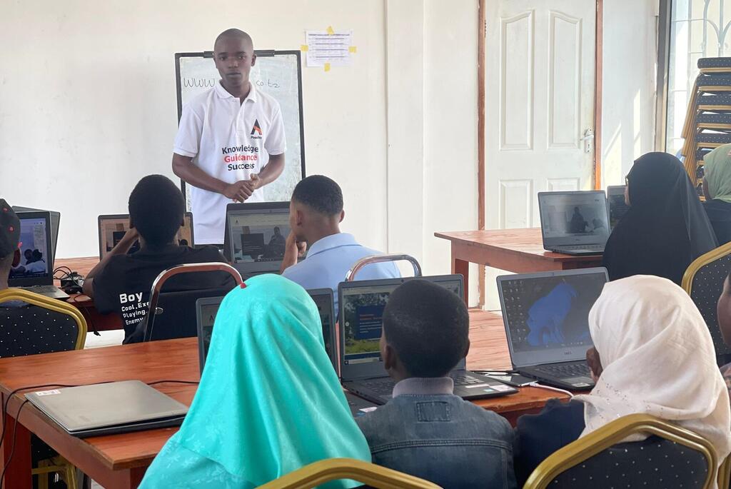 Mwalimu mmoja nchini Tanzania anasimama mbele ya darasa la wanafunzi wanaotumia kompyuta ndogo kwa ajili ya kikao cha elimu ya ICT.