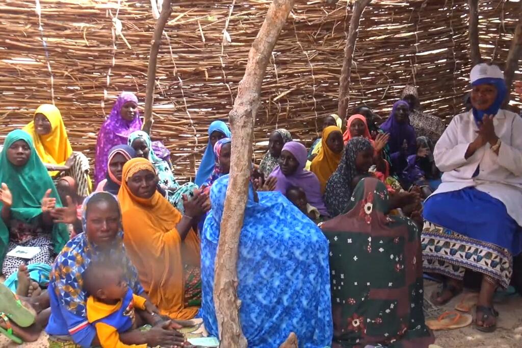 Kikundi cha wanawake na watoto wamekusanyika karibu na mhudumu wa afya wa WHO katika kliniki tembezi nchini Niger.