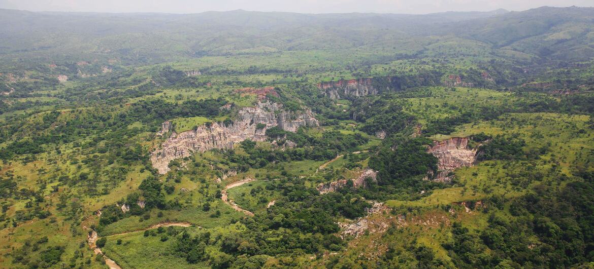 Aerial view of a river crossing in the Ituri hills of the DR Congo, showing a winding river through a lush green landscape with rocky outcrops.