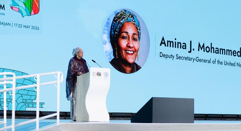 Amina Mohammed, Deputy Secretary-General of the United Nations, speaks at a podium during the World Urban Forum (WUF13) in Baku, Azerbaijan. A large screen behind her displays her portrait and name.