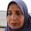 صورة مقربة لسيدة فلسطينية ترتدي حجابا أزرق، تبدو حزينة أمام خيمة في غزة.
