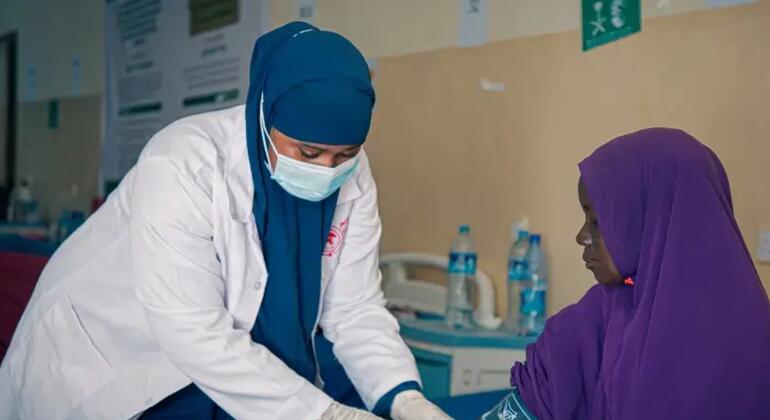 Mfanyakazi wa afya katika kanzu nyeupe na hijab ya bluu anachukua kipimo cha shinikizo la damu kutoka kwa mgonjwa aliye na hijab ya zambarau katika kliniki huko Somalia.