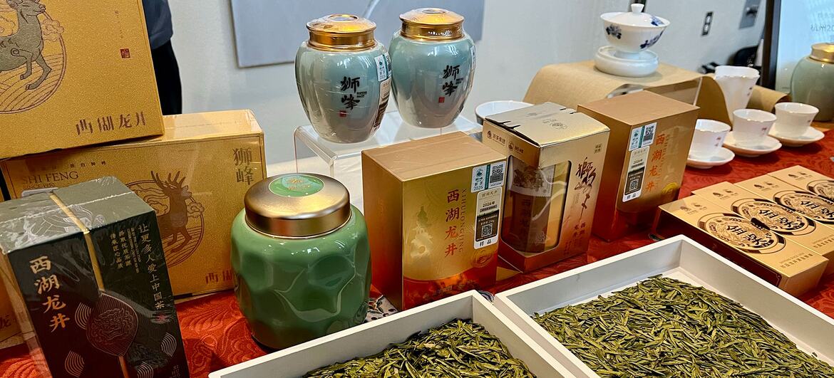 一张铺着红桌布的展示桌上陈列着中国龙井茶，包括白色托盘中的散装茶叶以及盒装和罐装的产品。