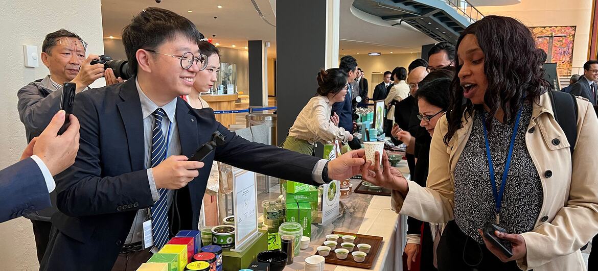 活动期间，一名身穿西装的男子在产品展示展位上向一名女子递上一杯茶。