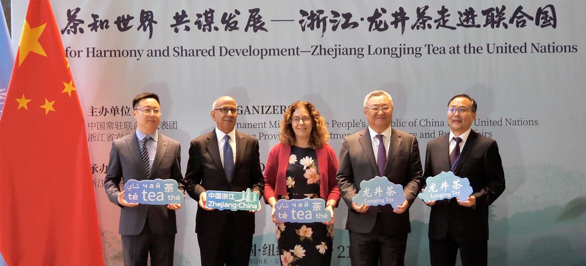 五位官员站在讲台前，手持中国国旗，举着写有“浙江 - 中国”和“龙井茶”的标语牌，参加联合国活动。